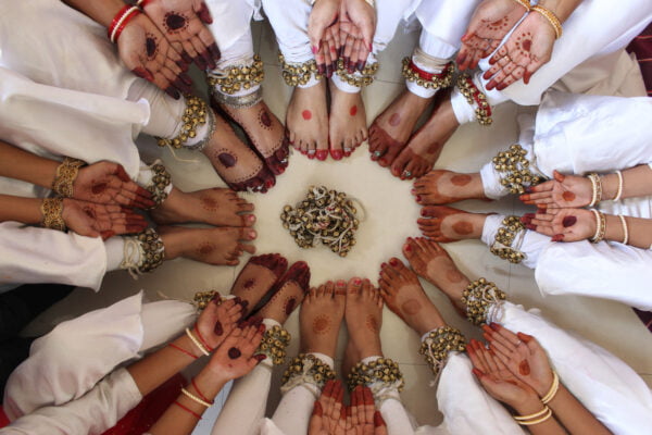 Kathak dancers in costumes and colored feet and hands sitting in a circle